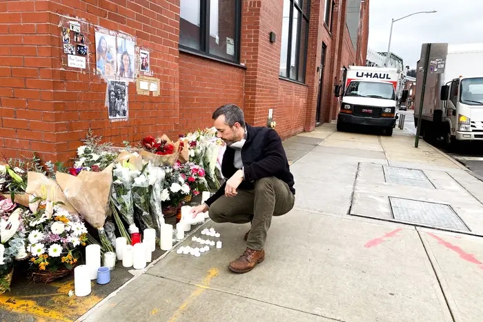 A man lights a candle at a memorial for a cyclist at a Brooklyn intersection.